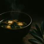 Ciotola di zuppa di miso su un tavolo con foglie verdi accanto