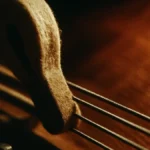 Primo piano su un martelletto rivestito di feltro che percuote tre corde di pianoforte in metallo